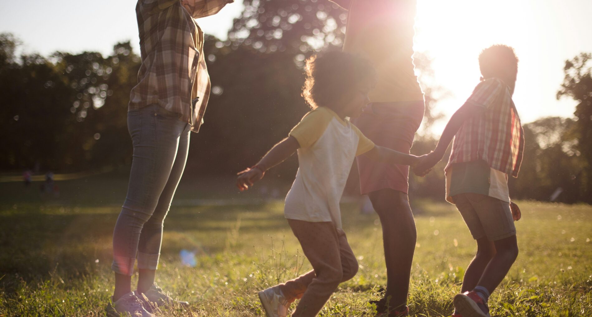 Parents with two young kids play in a field with a setting sun in the background