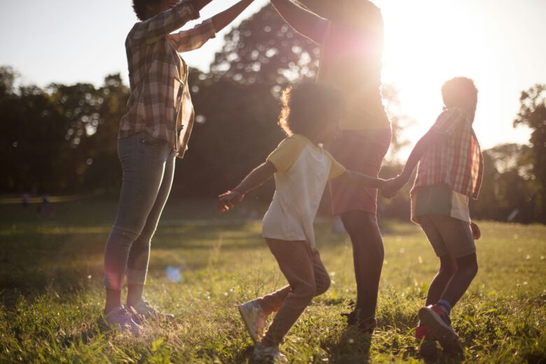 Parents with two young kids play in a field with a setting sun in the background