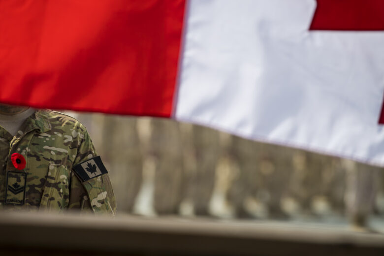 Veteran wearing a uniform and standing proudly in front of a flag, with a solemn expression and a clear background.