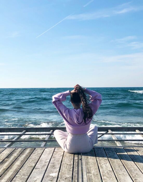 Woman seated crossed legged on a dock in front of blue ocean