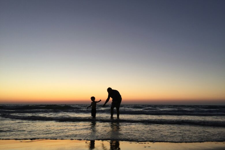 Adult and child on a beach at sunset